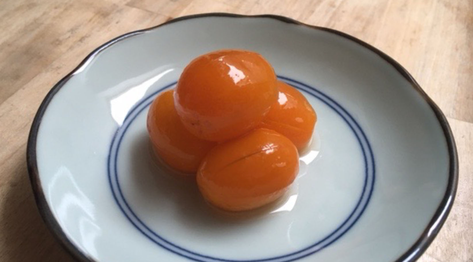 4 glasierte Kumquats auf einem kleinen Tellerchen mit blauem Rand